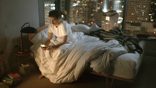 Joaquin Phoenix sitzt im Film Her auf eienmBett und schaut auf sein Smartphone