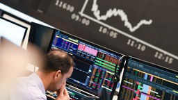 Ein Aktienhändler beobachtet auf dem Parkett der Frankfurter Wertpapierbörse vor der Tafel mit der fallenden Dax-Kurve seine Monitore.