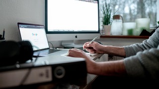 Jemand sitzt am heimischen Schreibtisch am Computer mit zwei Monitoren