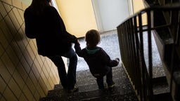 Frau läuft mit Kind an der Hand eine Treppe runter