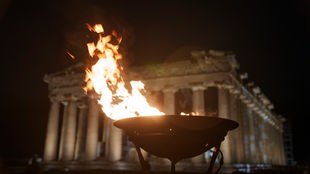 19.04.2024, Griechenland, Athen: Ein Kessel mit dem olympischen Feuer brennt vor dem antiken Parthenon-Tempel auf dem Akropolis-Hügel