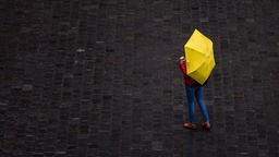 Frau steht mit gelbem Regenschirm auf grauem Untergrund