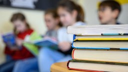 Bücher stehen auf einem Tisch. Im Hintergrund sind Kinder zu sehen