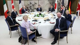 Teilnehmer des G7-Gipfels in Hiroshima sitzen an einem Tisch und lächeln in die Kamera.