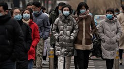 Passanten mit Mund-Nasen-Schutz auf einer Straße in Peking. 