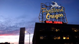 Das Schild "Portland, Oregon" ist beleuchtet, im Hintergrund das Wells Fargo Center-Gebäude in der Innenstadt von Portland.