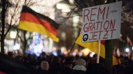 Teilnehmer einer Mahnwache rechter Gruppen stehen mit einem Schild mit der Aufschrift "Remigration Jetzt" vor dem Bundeskanzleramt in Berlin.