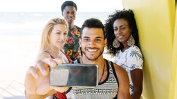 Zwei junge Männer und zwei junge Frauen machen ein Selfie am Strand. 