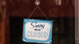 An einer Glasscheibe hängt ein Vintage-Schild mit der Aufschrift "Sorry, we're closed".