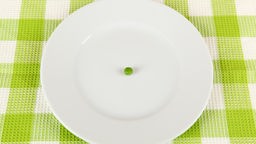 Eine grüne Erbse liegt auf einem weißen Teller. 