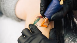 Eine Tätowiererin sticht ein Pfirsich-Tattoo auf den Unterarm einer Kundin