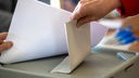 Eine Hand wirft einen Stimmzettel in eine Wahlurne