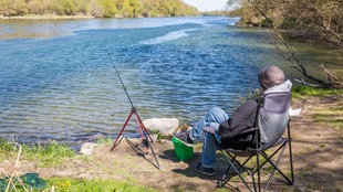 Ein junger Mann nutzt das sonnige Wetter, um am Rhein zu Angeln und so den eigenen vier Wänden für einen Nachmittag zu entkommen.