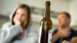 Ein junge Frau mit ihrem Vater, während im Vordergrund eine Bierflasche steht. 