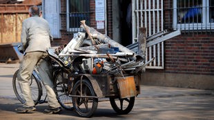 Ein Schrottsammler bringt auf einem Anhänger an einem alten Fahrrad gesammeltes Altmetall auf den Hof eines Schrottverwerters. 