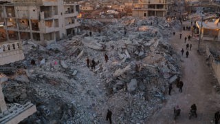 Syrien, Jinderis: Menschen gehen an eingestürzten Gebäuden vorbei. 