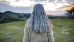 Frau mit langen, grauen Haaren blickt auf die Landschaft. 