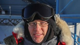 Porträtfoto des Astrophysikers Robert Schwarz, der die warme Fellkapuze seiner Winterjacke über seinem Kopf trägt.