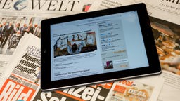 Tablet-Computer mit einer Online-Zeitung auf dem Bildschirm liegt auf einem Tisch mit Zeitungen