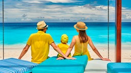 Familie sitzt am Strand und blickt auf das Meer