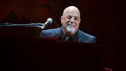 Billy Joel sitzt an einem schwarzen Flügel während seiner 100. Performace im Madison Square Garden in New York City, USA.