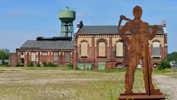 Außenansicht der Zeche Dinstlaken-Lohberg: Gebäude, Wasserturm, Metallskulptur Bergarbeiter.