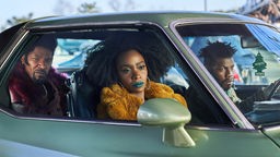 Filmszene aus "They Cloned Tyrone", zwei Männer und eine Frau sitzen in einem Auto.