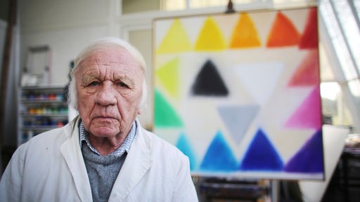 Der Zero-Künstler Heinz Mack sitzt vor einem Gemälde.
