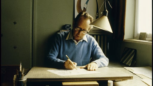 Der Comicbuch-Zeichner Maurice De Bevere alias "Morris" sitzt an einem Schreibtisch.