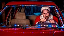Szene aus: "Schrille Nacht", als Weihnachtsmann verkleiderterter Mann fährt Auto.