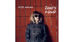 Auf dem Cover für ihr neues Album "James Bond" steht Kitty Solaris im Trenchcoat und Sonnenbrille vor einer roten Backsteinwand.