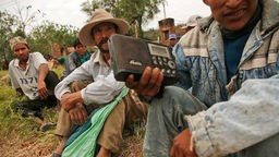 Bolivianer sitzen auf einer Wiese und hören Radio.