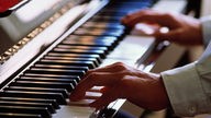 Symbolbild: Ein Pianist spielt Klavier, Detailaufnahme mit Blick auf die Hände.