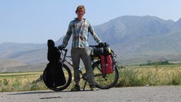 Phillip mit Fahrrad, Gepäck und Berge im Hintergrund