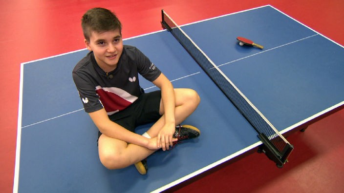 Ein Junge sitzt auf einer Tischtennisplatte.