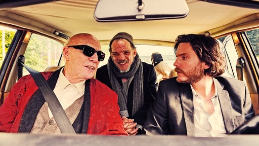 Sebastian Zöllner (Daniel-Brühl, r) mit Kaminski (Jesper Christensen, l) und Karl Ludwig (Denis Lavant) im Auto untewegs.