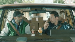 Zwei Männer sitzen in einem Auto und sprechen miteinander