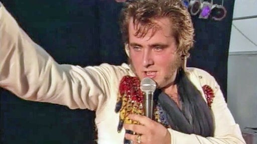 Elvisimitator singt ins Mikrofon und macht eine Elvis-Geste