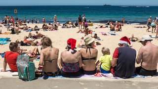 Man erkennt eine Menge an Menschen am Strand in Weihnachtsmützen.