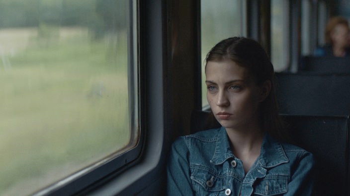 Eine junge  Frau sitz im Zug und schaut aus dem Fenster