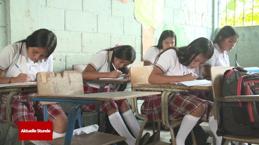 Mädchen in Schuluniformen gekleidet sitzen an ihren Schreibtischen und schreiben in Hefte.