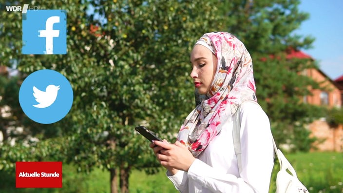 Eine Frau mit Kopftuch geht an Bäumen vorbei und schaut auf ihr Handy. Vor ihr befinden sich die verzerrten Logos von Facebook und Twitter