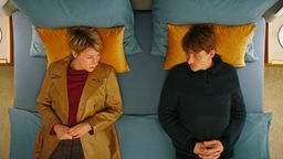 Ein Mann und eine Frau (Corinna Harfouch, l. und Daniel Sträßer, r.) liegen nebeneinander in einem Bett und schauen sich gegenseitig an.