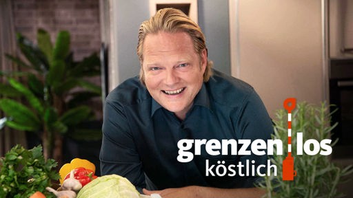 Björn Freitag lehnt auf einem Tisch, auf dem Rosmarin und eine Kiste mit Gemüse stehen, auf dem Bild der Schriftzug "grenzenlos köstlich mit Björn Freitag"