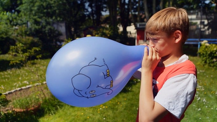 Ein Kind pustet einen Luftballon auf