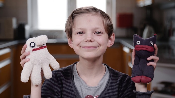 Olivia sitzt an einem Tisch, auf dem viele Sockenpuppen verteilt sitzen