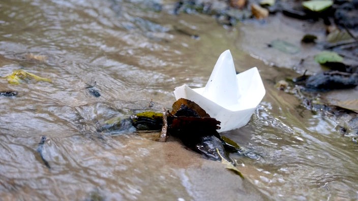 Ein selbstgebasteltes Papierboot treibt auf einem kleinen Bach