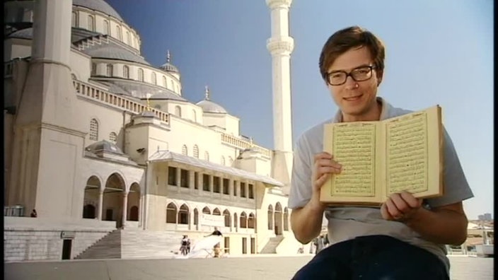 Ralph sitzt mit einem Buch vor einer großen Moschee