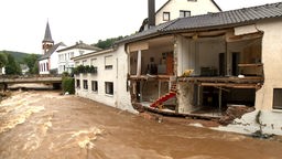 Ein übertretener Fluss und ein Haus, dessen eine Hälfte komplett weggerissen wurde.