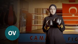 Frau mit Kopftuch steht vor einem Boxring in entsprechender Pose und mit Boxhandschuhen.
